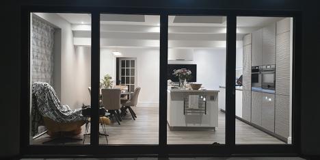 brightly lit kitchen and dining area viewed through bi-fold glass doors at night