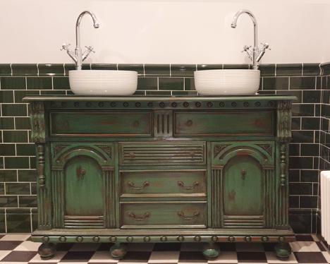 antique dresser with two counter-top basins and taps installed on a glass top.