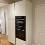 Pair of tall housings with fridge freezer to the left and ovens to the right of a vertical handleless rail.