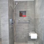 Walk-in shower area with wet room base, tiled in grey porcelain, featuring Hansgrohe shower, Kudos screen and tiled niche