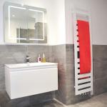 Grey tiled bathroom with illuminated mirror cabinet above a wall hung basin vanity unit and tall towel heating radiator