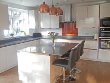 Magnolia high gloss handleless kitchen with copper handle trims and grey quartzstone worktop 