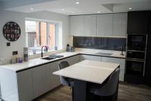 Handleless, quartz-topped, L-shaped kitchen with 2 stools either side of a central island 
