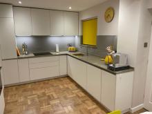Handleless kitchen in white and grey with wood effect parquet style flooring.